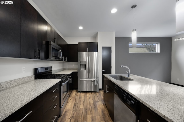 kitchen featuring light wood finished floors, appliances with stainless steel finishes, dark cabinetry, hanging light fixtures, and a sink