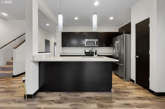 kitchen featuring light wood finished floors, a peninsula, a sink, stainless steel appliances, and decorative light fixtures