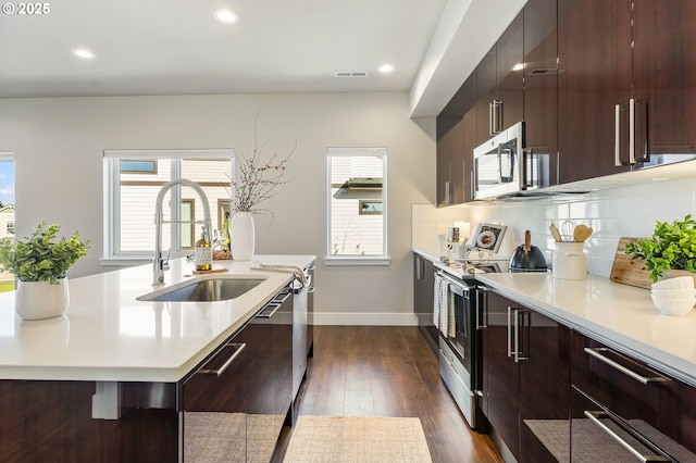 kitchen featuring dark wood-style floors, stainless steel appliances, tasteful backsplash, light countertops, and a sink
