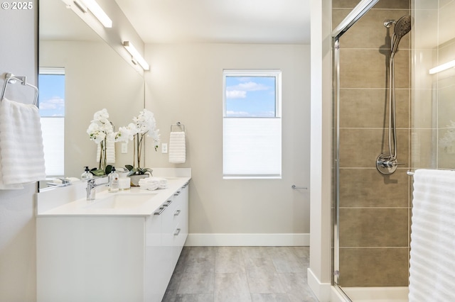 bathroom featuring a sink, a tile shower, baseboards, and double vanity