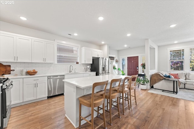 7510 NW Lauren Ave, Portland, OR 97229 - kitchen featuring appliances with stainless steel finishes, a kitchen breakfast bar, decorative backsplash, light wood-style floors, and a kitchen island