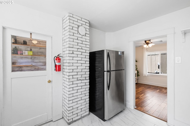 kitchen with freestanding refrigerator, a ceiling fan, light marble finish flooring, and baseboards