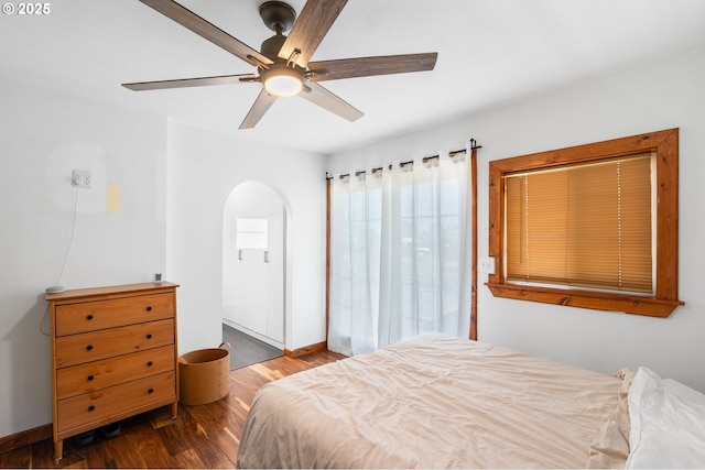 bedroom featuring wood finished floors, arched walkways, a ceiling fan, and baseboards