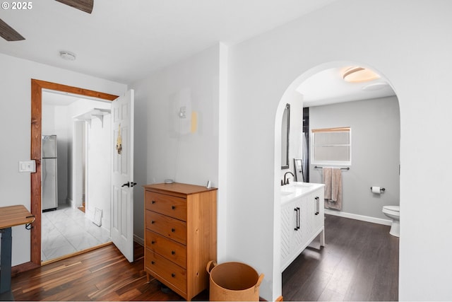 hallway featuring dark wood finished floors, arched walkways, and baseboards
