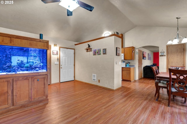 kitchen featuring arched walkways, lofted ceiling, light countertops, hanging light fixtures, and brown cabinetry