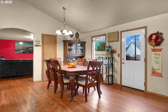 dining room featuring lofted ceiling, arched walkways, wood finished floors, and an inviting chandelier