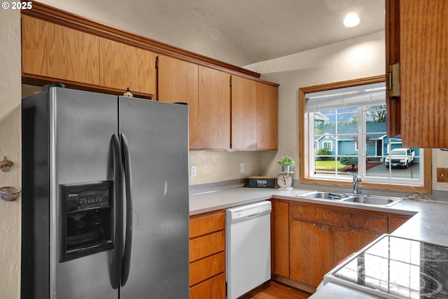 kitchen featuring stainless steel fridge, brown cabinetry, dishwasher, light countertops, and a sink