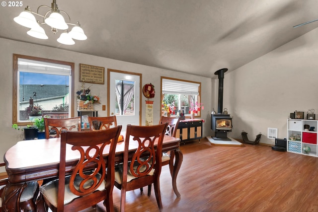 dining space with lofted ceiling, wood finished floors, a wood stove, and a chandelier