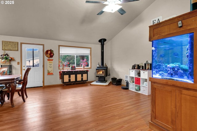 living room featuring a ceiling fan, lofted ceiling, a wood stove, and light wood finished floors