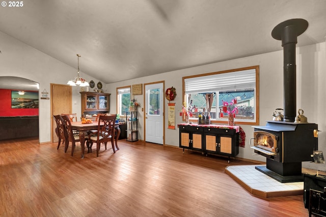 dining room featuring lofted ceiling, wood finished floors, a wood stove, and a healthy amount of sunlight