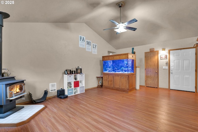 living room with a wood stove, ceiling fan, light wood-style flooring, and vaulted ceiling