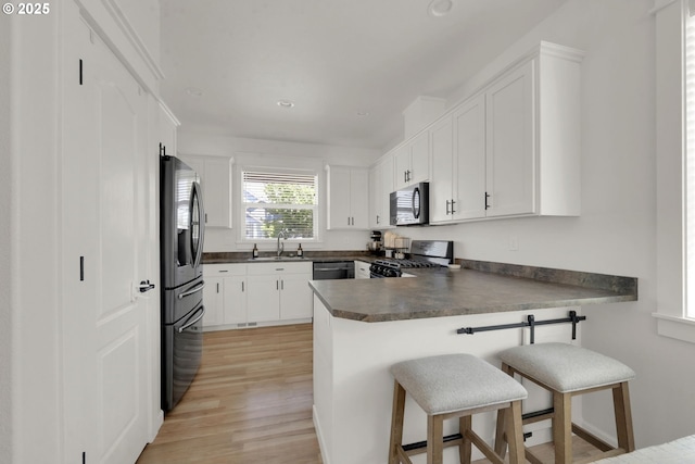 1027 Turtledove Loop, Lebanon, OR 97355 - kitchen with stainless steel appliances, dark countertops, a peninsula, a breakfast bar, and light wood finished floors