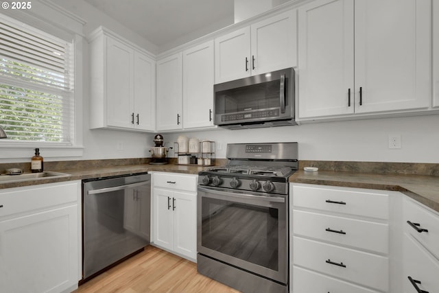 1027 Turtledove Loop, Lebanon, OR 97355 - kitchen with stainless steel appliances, dark countertops, white cabinets, and light wood-type flooring