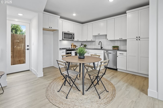 kitchen with appliances with stainless steel finishes, white cabinetry, sink, backsplash, and light hardwood / wood-style floors