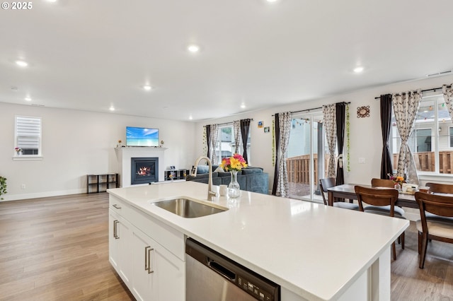 kitchen with dishwasher, an island with sink, sink, white cabinets, and light hardwood / wood-style floors