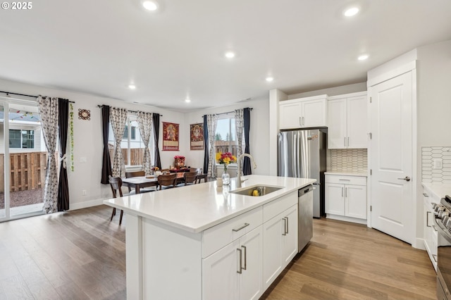 kitchen with white cabinetry, sink, a kitchen island with sink, light hardwood / wood-style floors, and stainless steel appliances