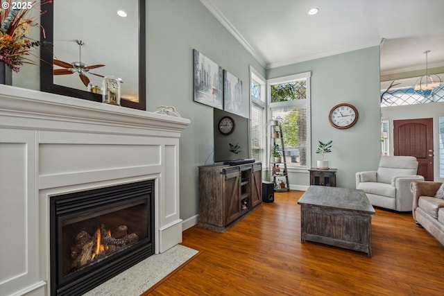 living area featuring crown molding, wood finished floors, a ceiling fan, a fireplace with flush hearth, and recessed lighting