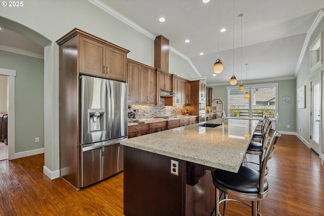 kitchen featuring stainless steel appliances, arched walkways, ornamental molding, a kitchen island with sink, and baseboards