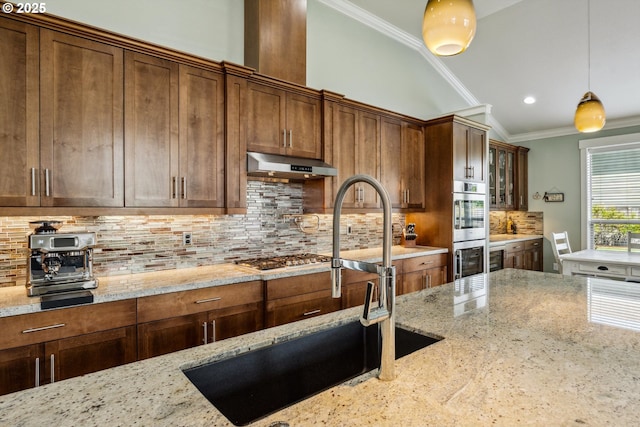 kitchen with under cabinet range hood, crown molding, light stone counters, decorative light fixtures, and a sink