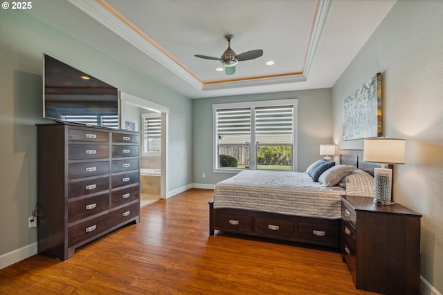 bedroom with a tray ceiling, wood finished floors, crown molding, baseboards, and connected bathroom