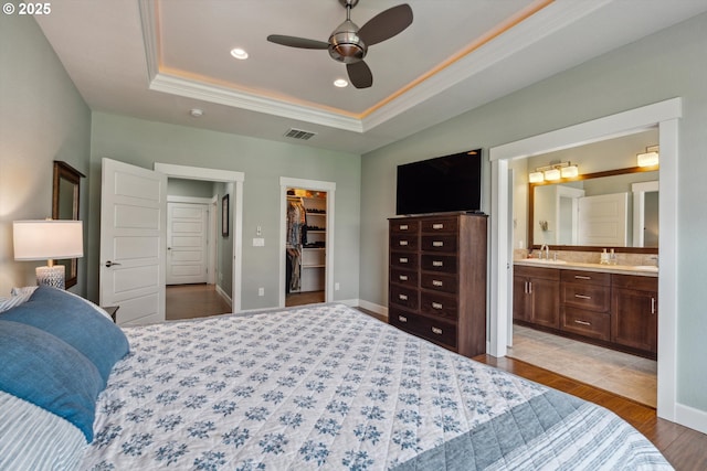 bedroom with ornamental molding, a spacious closet, a sink, a tray ceiling, and wood finished floors