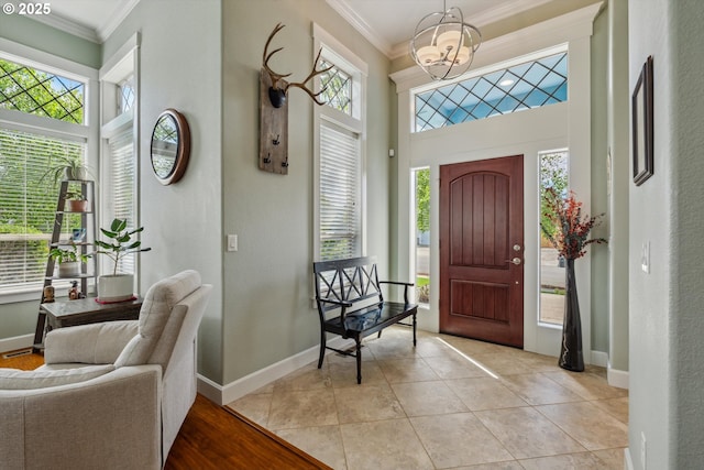 foyer with crown molding, healthy amount of natural light, a chandelier, baseboards, and a towering ceiling