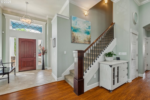 entryway featuring light wood finished floors, stairway, crown molding, baseboards, and a chandelier