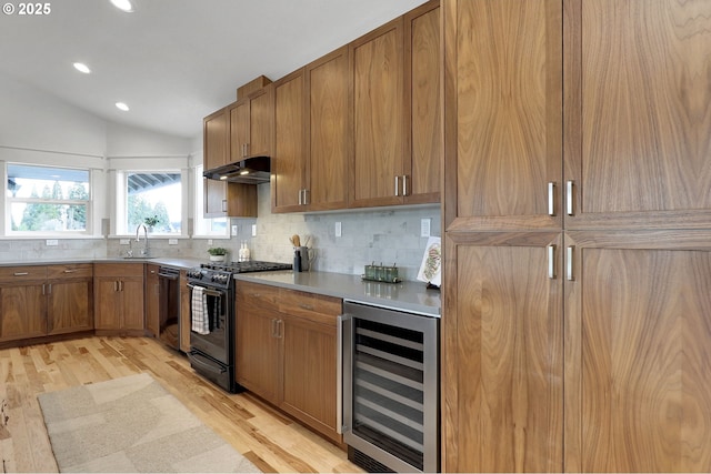 kitchen with wine cooler, light wood-type flooring, under cabinet range hood, a sink, and black appliances