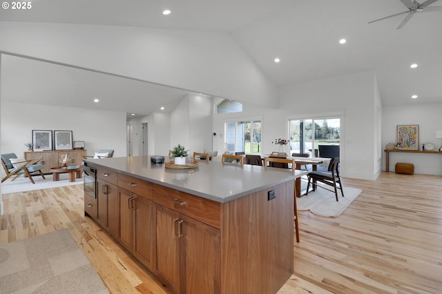 kitchen with light wood-style floors, high vaulted ceiling, a kitchen bar, a center island, and recessed lighting
