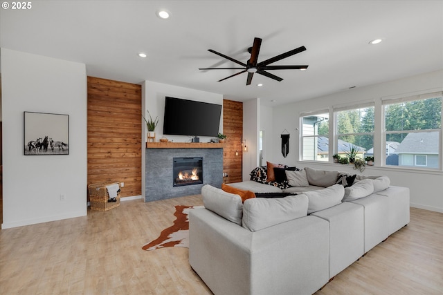 living area featuring a ceiling fan, a glass covered fireplace, recessed lighting, light wood-style floors, and baseboards
