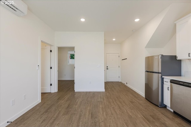 kitchen featuring appliances with stainless steel finishes, a wall unit AC, white cabinetry, light countertops, and light wood-style floors