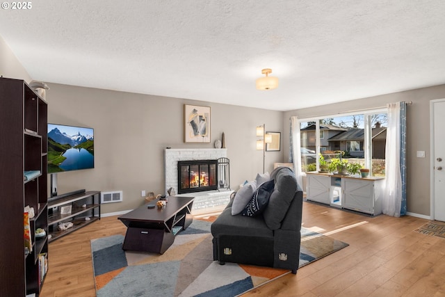 living area with visible vents, a fireplace, a textured ceiling, and wood finished floors