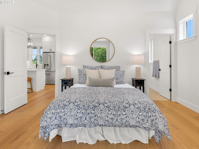 90190 Hobie Rd, Warrenton, OR 97146 - bedroom with stainless steel fridge with ice dispenser, multiple windows, light wood finished floors, and a chandelier