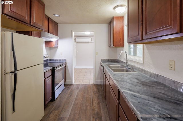 kitchen with sink, a textured ceiling, a wall unit AC, white refrigerator, and stainless steel electric range