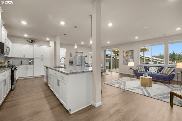 kitchen with stainless steel microwave, range with gas cooktop, open floor plan, wood finished floors, and a sink