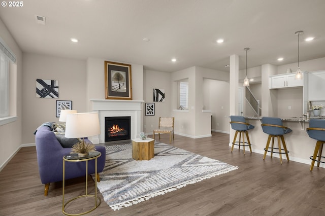 living area with recessed lighting, stairway, a lit fireplace, and wood finished floors