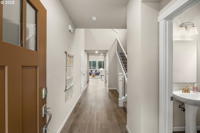 hall featuring wood finished floors, baseboards, and a sink