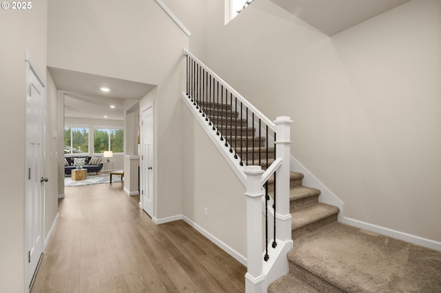 stairway featuring recessed lighting, baseboards, a towering ceiling, and wood finished floors