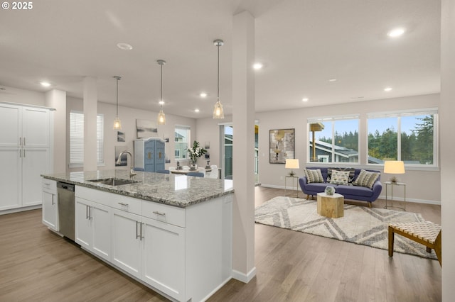 kitchen featuring a kitchen island with sink, a sink, open floor plan, stainless steel dishwasher, and light wood-type flooring