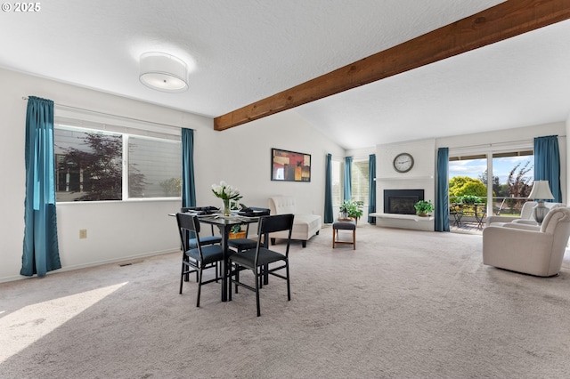 dining room with a textured ceiling, visible vents, a large fireplace, carpet floors, and vaulted ceiling with beams