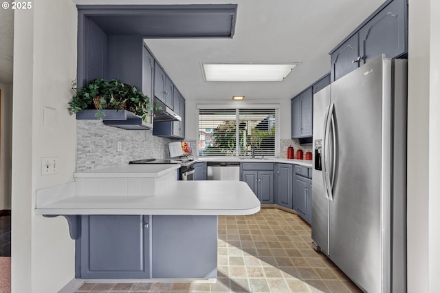 kitchen with appliances with stainless steel finishes, gray cabinets, a peninsula, decorative backsplash, and under cabinet range hood