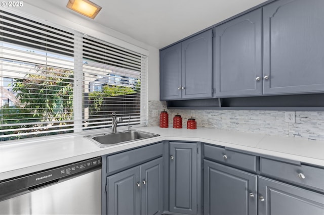 kitchen with stainless steel dishwasher, a sink, gray cabinets, and light countertops