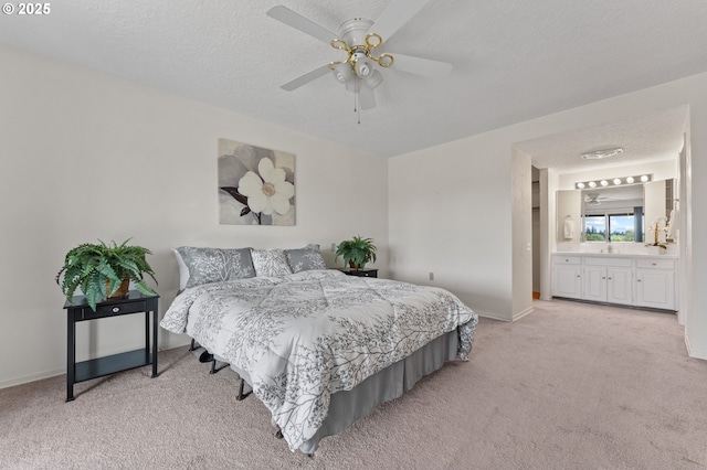 bedroom featuring baseboards, ceiling fan, light colored carpet, a textured ceiling, and ensuite bath