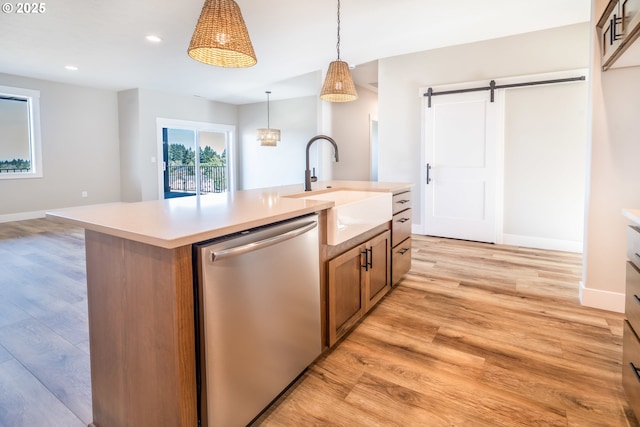 kitchen with pendant lighting, sink, a kitchen island with sink, stainless steel dishwasher, and a barn door