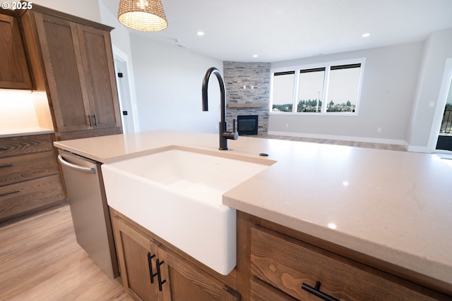 kitchen with sink, light hardwood / wood-style flooring, decorative backsplash, a stone fireplace, and stainless steel dishwasher