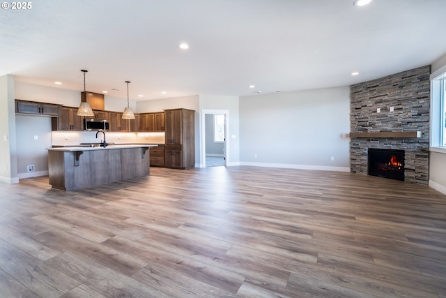 kitchen with a fireplace, sink, hanging light fixtures, a center island with sink, and light wood-type flooring