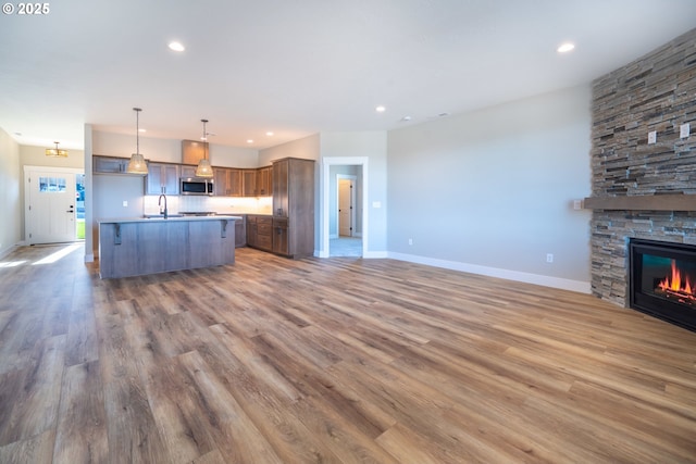 kitchen with decorative light fixtures, dark hardwood / wood-style flooring, a kitchen island with sink, and a stone fireplace