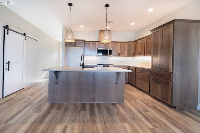 kitchen featuring sink, hanging light fixtures, tasteful backsplash, an island with sink, and a barn door