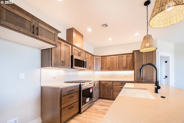 kitchen featuring pendant lighting, sink, decorative backsplash, stainless steel appliances, and light hardwood / wood-style flooring