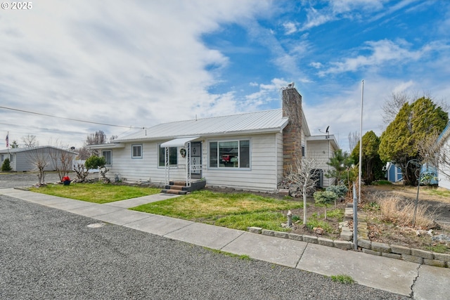 ranch-style home with a front lawn, a chimney, and metal roof